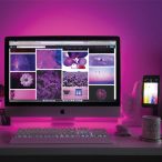 iMac computer and iPhone phone showing pictures of flowers, balloons and water. Behind the screens, the wall reflects purple